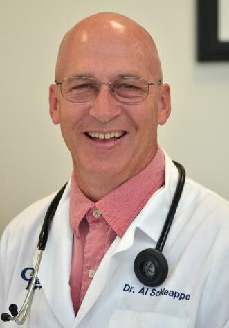 A man in white coat and glasses smiling for the camera.