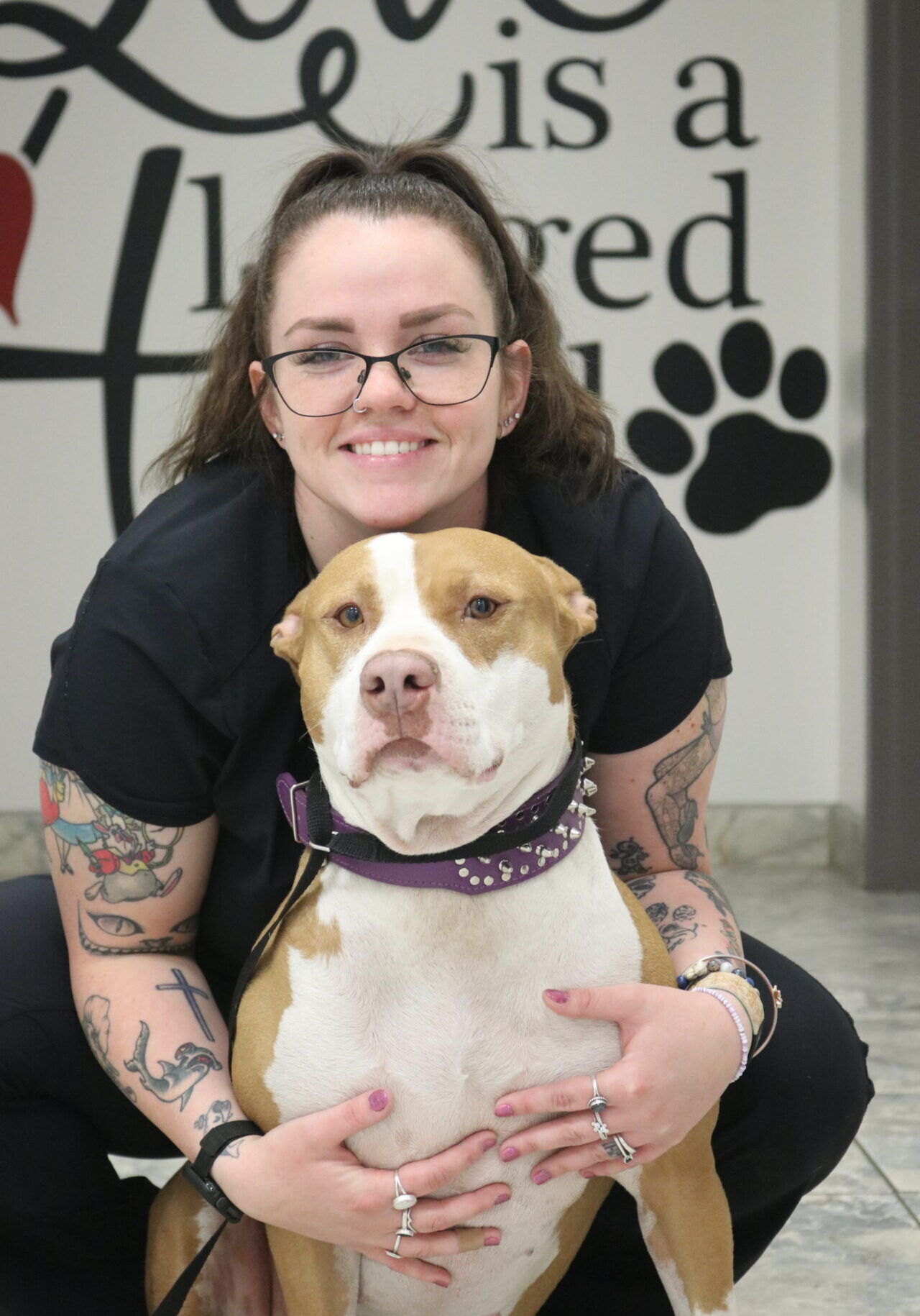 A woman with tattoos and glasses holding a dog.