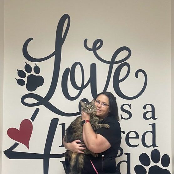 A woman holding a cat in front of a wall with lettering.